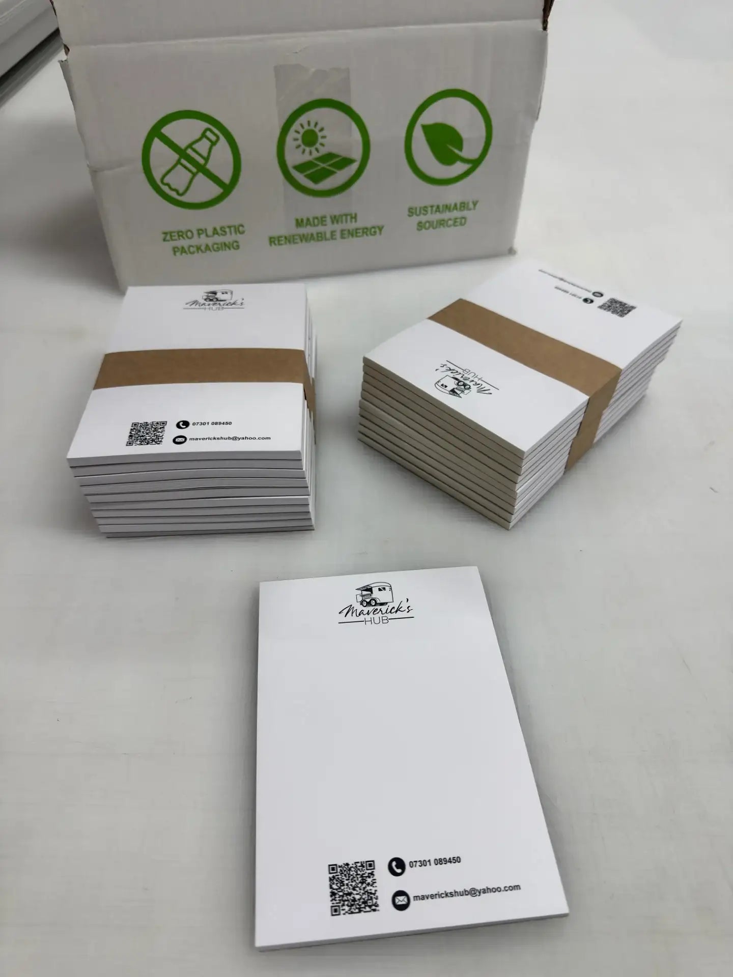 A6 notepads with branded design stacked on a table, eco-friendly packaging box in background.