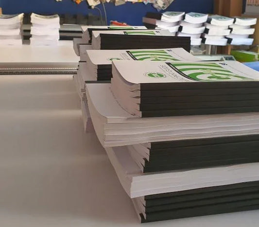 Stacked perfect bound booklets with printed covers on a print shop table