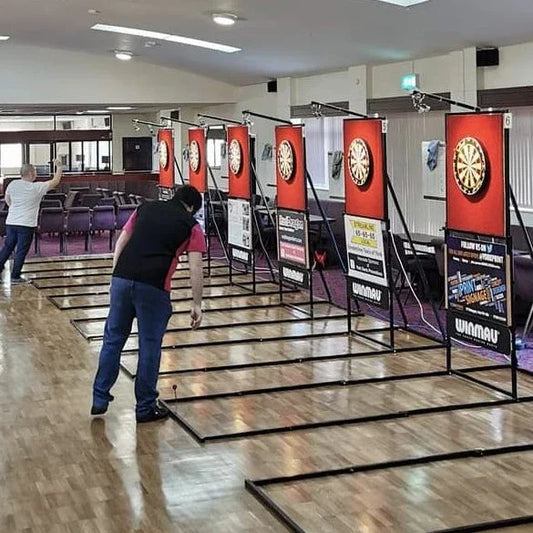Indoor darts tournament with multiple dartboards, players, and printed banners on display.