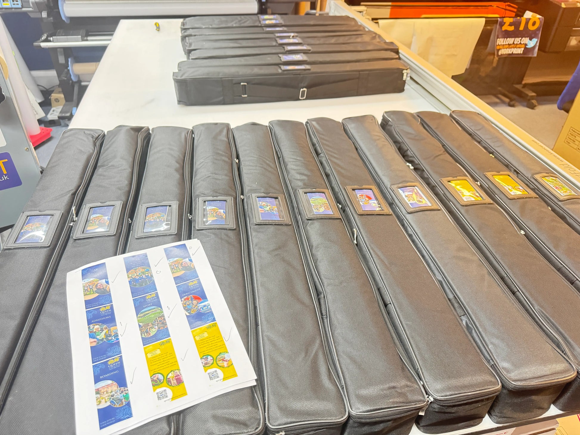 Black banner carry cases neatly lined up on a print shop table with printed labels.