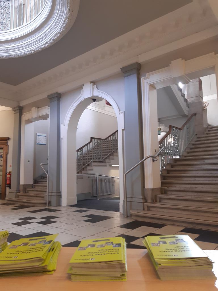 Historic library interior with grand staircase, arched entryway, and brochures on a table