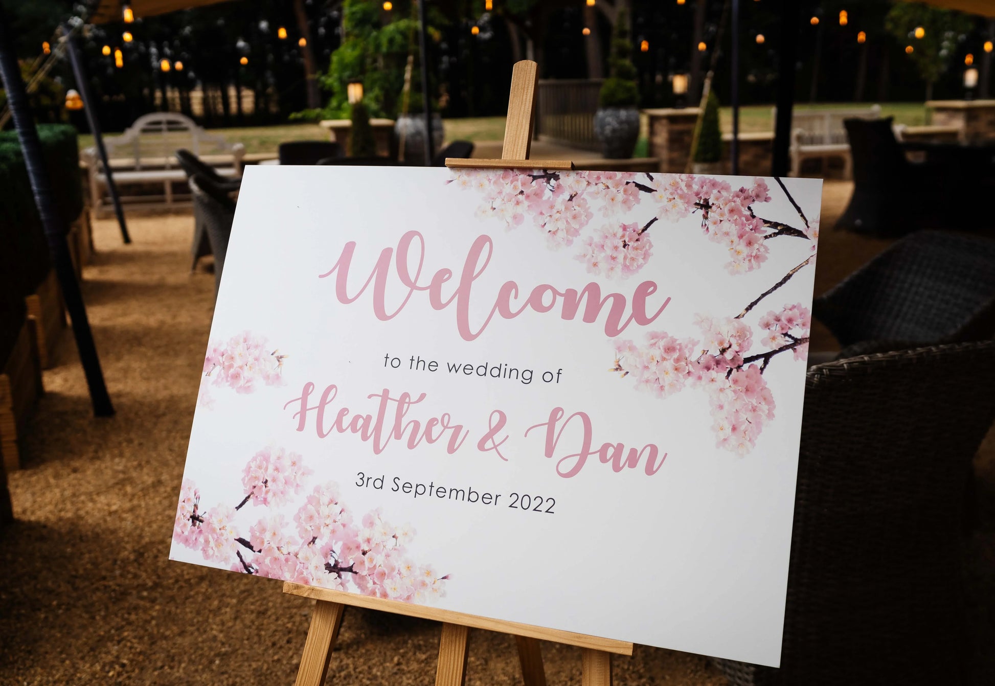 Wedding welcome sign with pink cherry blossoms on easel, outdoor venue setting