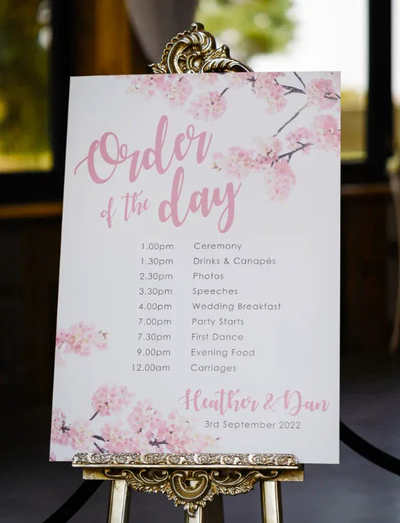 Wedding order of the day sign with pink floral design on ornate easel
