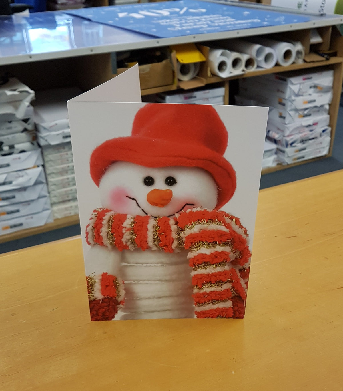 Folded Christmas card with full-colour snowman photo printed on 350gsm silk, standing on the counter at York Print