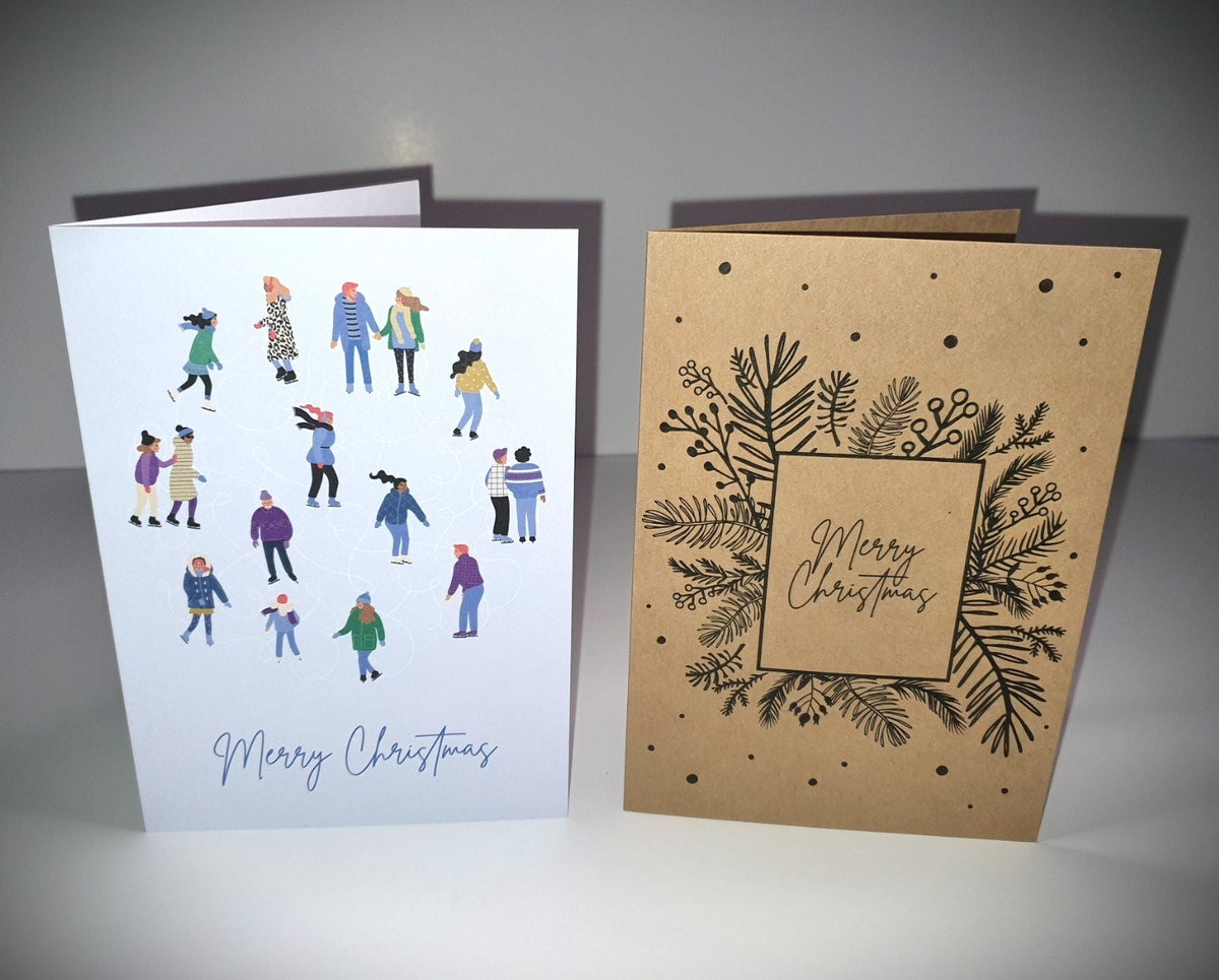 Two printed folded Christmas cards with envelopes from York Print – white ice-skaters design and kraft foliage design, both reading Merry Christmas